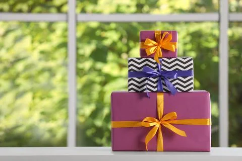 Stack of beautifully wrapped gift boxes on white table  near window. Space fo Stock Photos