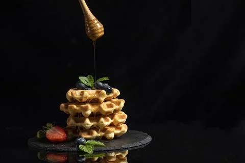 Stack of Belgian waffles with strawberries and mint leaves with pouring honey on Stock Photos