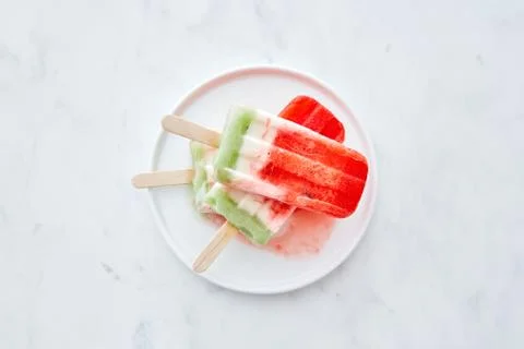 A stack of berry melting ice cream lolly in a white plate on a gray marble Stock Photos