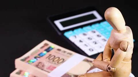 A stack of bills, a calculator and a wooden doll : rotating Stock Footage 322039924