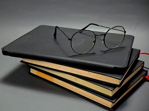 A stack of black journals and notebooks with round glasses resting on the t.. Foto stock
