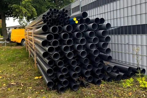 A stack of black pipes leans against a wall near a construction site. Stock Photos