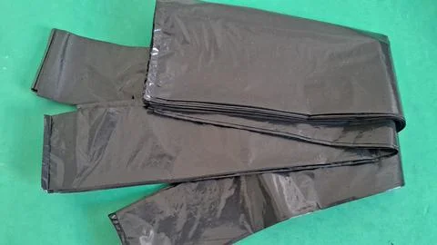 Stack of black plastic garbage bags on a green surface Stock Photos