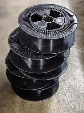 Stack of black plastic spools on concrete floor in indoor setting with neut.. Foto stock
