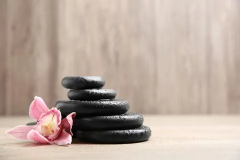 Stack of black spa stones with flower on wooden background. Space for text Stockfoto's