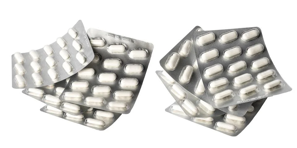 A stack of blisters with oblong white tablets on a white background. Stock Photos