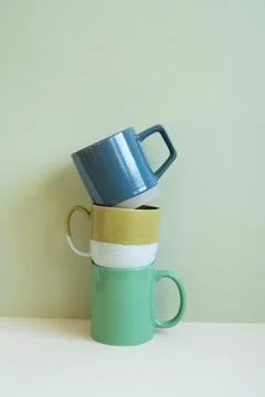 Stack of blue and green mug cups on white table. mint wall background Stock Photos