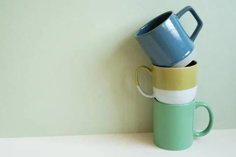 Stack of blue and green mug cups on white table. mint wall background. cop... Stock Photos