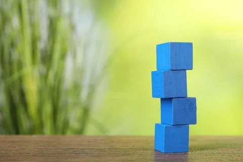 Stack of blue cubes on wooden table against blurred background. Space for tex Stock Photos