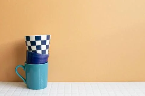 Stack of blue cups on white table. orange wall background. copy space Stac... Stock Photos