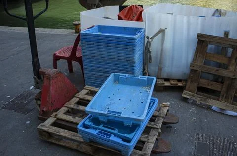 Stack of blue fish crates and pallet jack on concrete pier at harbor for fi.. Photos