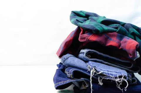 Stack of blue jeans and plaid shirts on white background Stock Photos