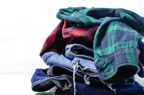 Stack of blue jeans and plaid shirts on white background Stock Photos