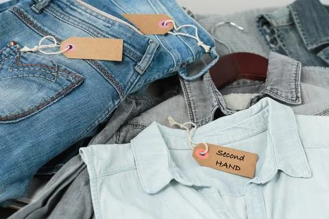 Stack of blue jeans, shirts and tag with inscription second hand Stock Photos