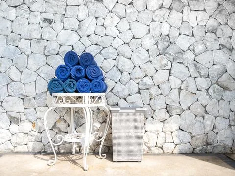 Stack of blue rolled towels on white metal table beside basket, against sto.. Stock Photos