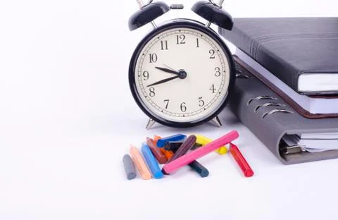 Stack of book with ticking vintage clock and colorful crayon on white table.n Foto stock