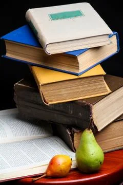 Stack of books and apple and pear on dark black background. Back to school Foto stock