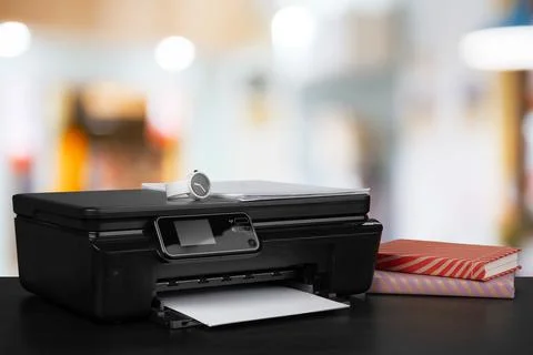 Stack of books and home printer against blurred background Stock Photos