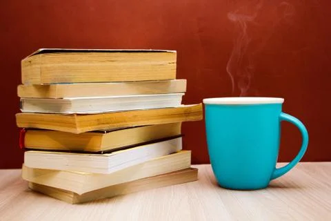 A stack of books and a hot drink in a blue mug on wooden table, Stock Photos