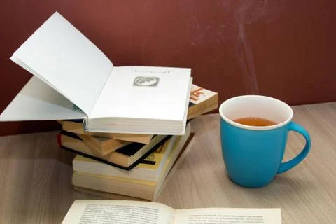 A stack of books and a hot drink in a blue mug on wooden table, Stock Photos