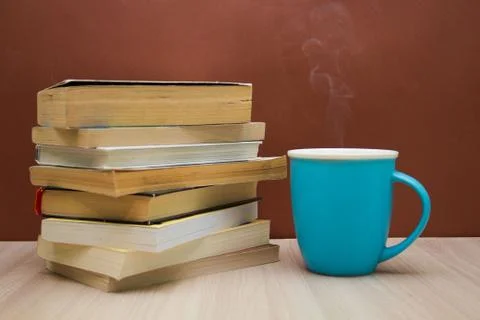 A stack of books and a hot drink in a blue mug on wooden table, Stock Photos