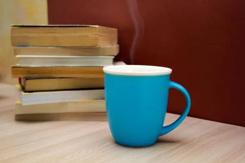 A stack of books and a hot drink in a blue mug on wooden table, Stock Photos