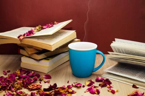 A stack of books and a hot drink in a blue mug on wooden table with rose peta Foto stock