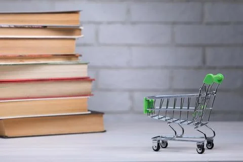 Stack with books and mini shopping cart on table, education concept, tuitio.. Stock Photos