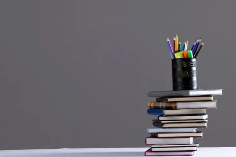 Stack of books and notebooks with pencil container on top and copy space on grey Foto stock