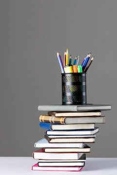 Stack of books and notebooks with pencil container on top and copy space on grey Foto stock