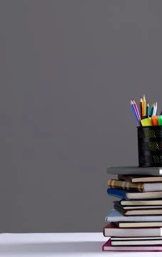Stack of books and notebooks with pencil container on top and copy space on grey Foto stock