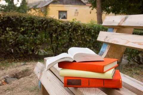 Stack of books and Open hardback book on blurred nature landscape backdrop. Copy Stock Photos