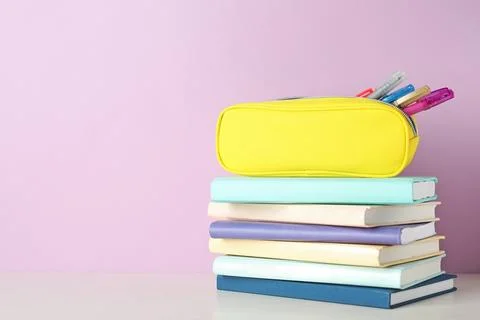 Stack of books and pen case on table against color background. Space for text 写真素材