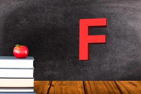 Stack of books and red apple on chalkboard background with F grade Foto stock