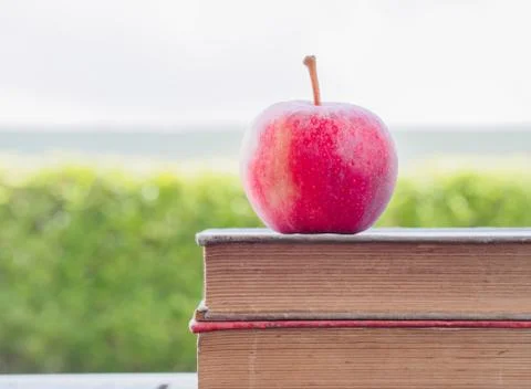 Stack of books and red apple on wooden table Stock Photos