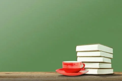 A stack of books and a red coffee cup with saucer on a wooden table against.. Stock Photos