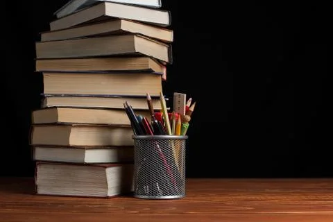 A stack of books and a stand for pens on a table, on a black background. Stock Photos
