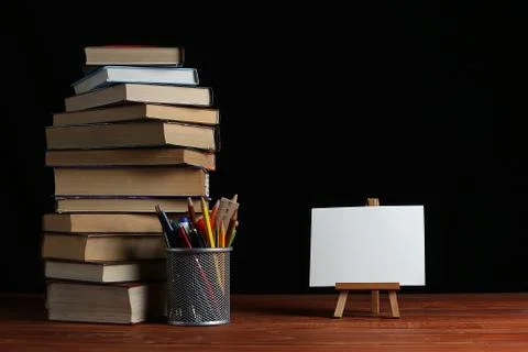 A stack of books and a stand for pens on a table, on a black background. A sm Stock Photos