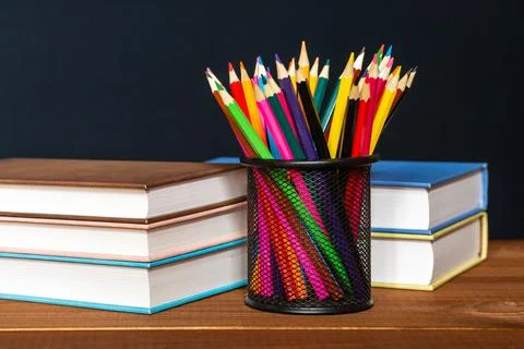 A stack of books and a stand for pens on a table, on a black background. Stock Photos