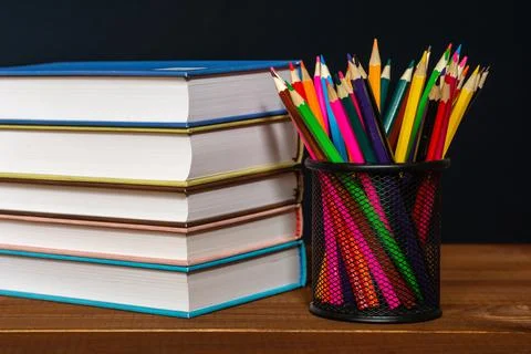A stack of books and a stand for pens on a table, on a black background. Stock Photos