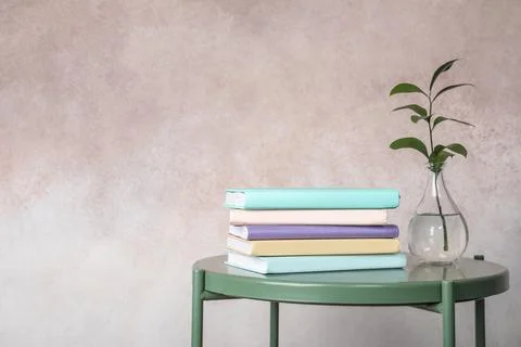 Stack of books and vase on table against color background. Space for text Foto stock