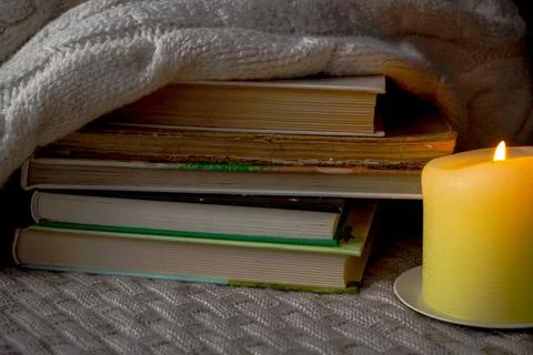 A stack of books and a warm sweater on a knitted plaid by candlelight Foto stock