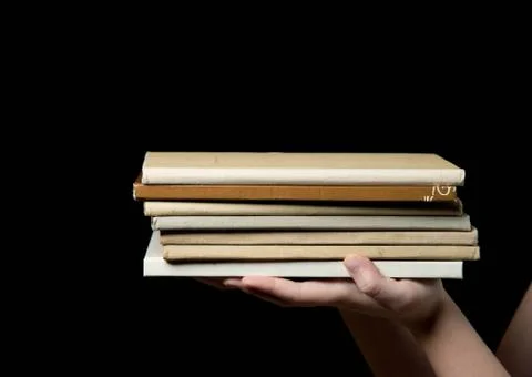 Stack of books in a children's hand on dark background Stock Photos