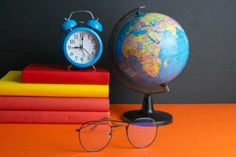 A stack of books, clock, world globe, and women's glasses in the foreground,  Stock Photos