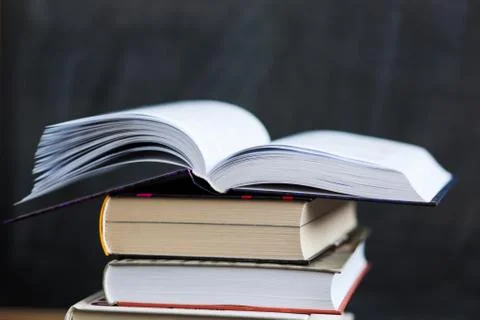 Stack of books close up with chalkboard in background. One book is opened Stock Photos