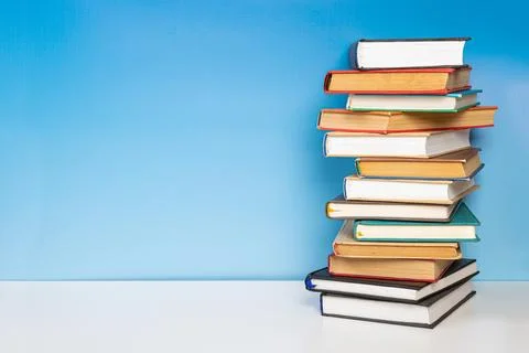 Stack of books in the colored cover lay on the wooden  table and blue backr.. 写真素材
