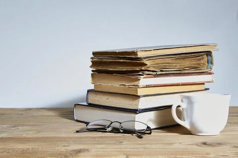 Stack of books with a cup and glasses next to it. Space for text. The concept of Stock Photos