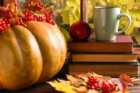 Stack of books, cup with aromatic tea, pumpkin and dry leaves on wooden win.. Foto stock
