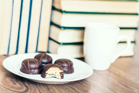 Stack of books, cup of coffee and chocolate cookies white plate. Stock Photos