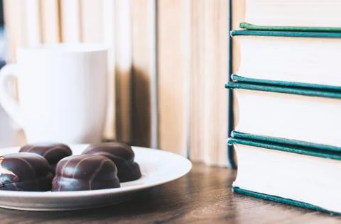 Stack of books, cup of coffee and chocolate cookies white plate. Stock Photos